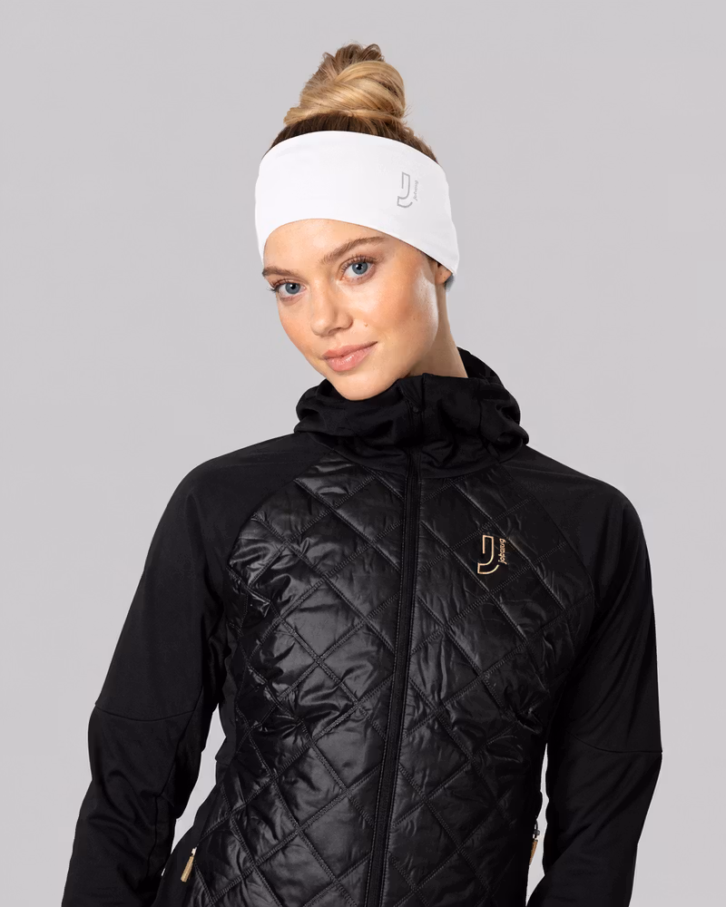 Woman wearing a white headband and black quilted Johaug jacket, posing against a gray background