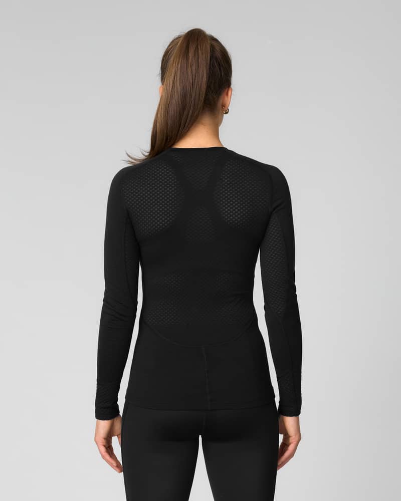 Back view of woman wearing a black long-sleeve baselayer top with mesh panel detailing