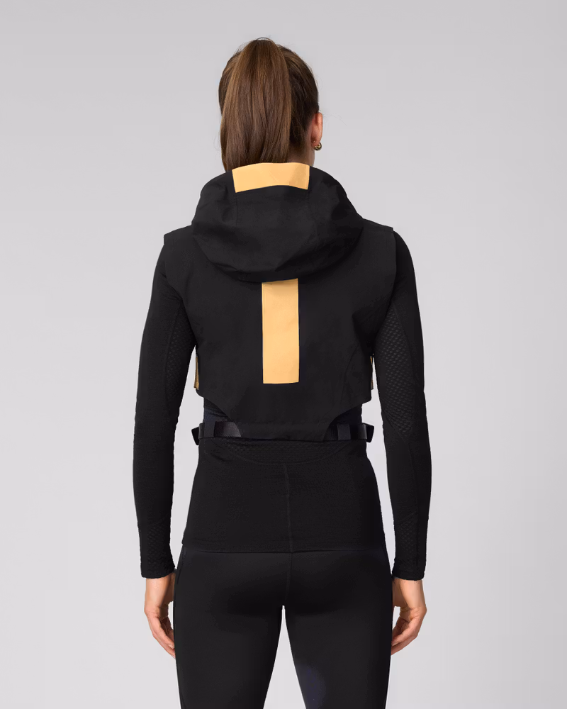 Back view of woman wearing a black hooded jacket with tan accent panel and adjustable straps