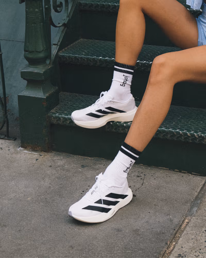 Close-up of legs wearing white running shoes with black stripes and white socks with black trim, seated on outdoor stairs