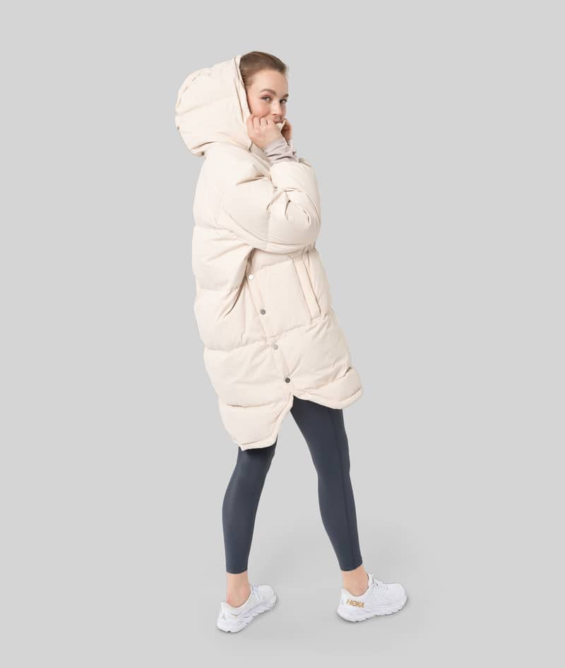 Side profile of a woman in the long off-white Johaug Adapt Down Poncho 2.0, showing its full coverage.