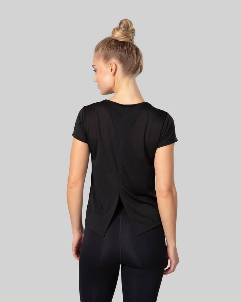 Back view of woman wearing a black Johaug short-sleeve t-shirt with crossed back design, studio photo