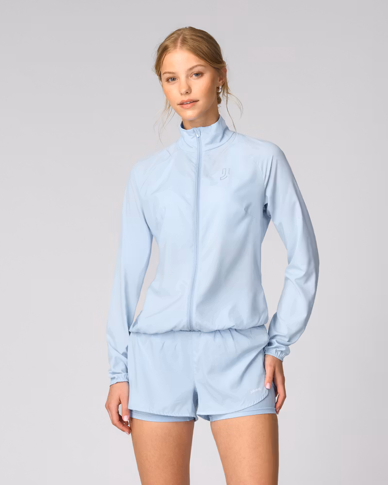 Woman wearing Johaug light blue Energy Jacket, a lightweight windbreaker for running.
