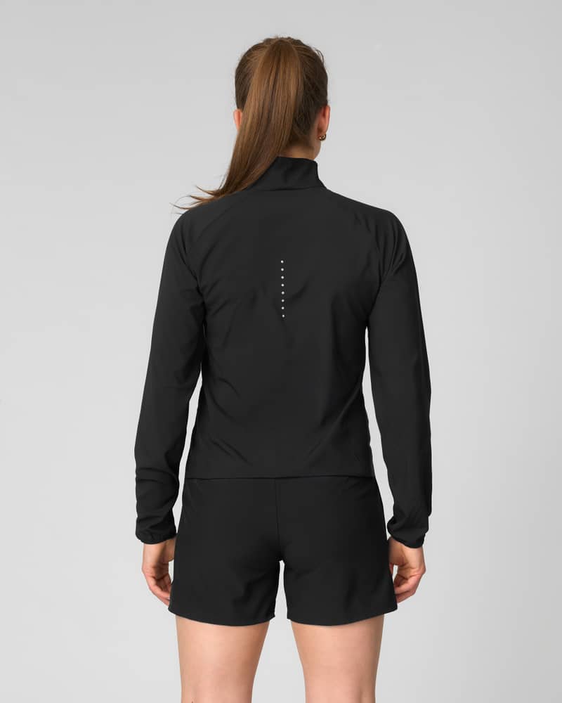 Back view of woman wearing a black Johaug long-sleeve zip jacket and black shorts, studio photo