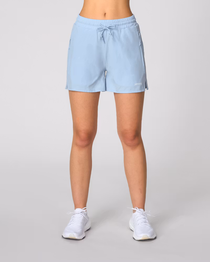 Front view of woman wearing light blue Johaug drawstring shorts and white sneakers, studio model photo