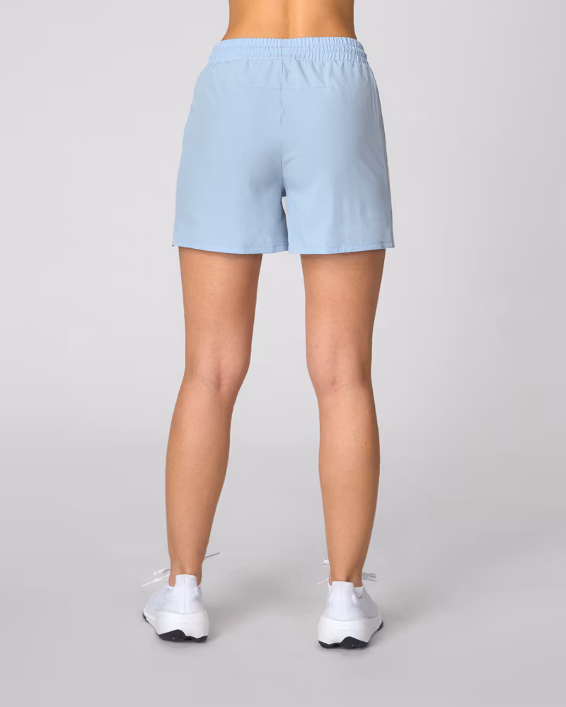 Back view of woman wearing light blue Johaug drawstring shorts and white sneakers, studio model photo