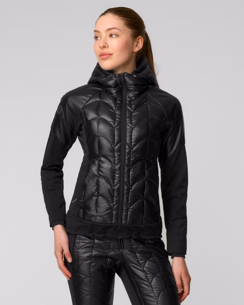 Woman wearing a glossy black quilted ski jacket, holding ski poles in falling snow