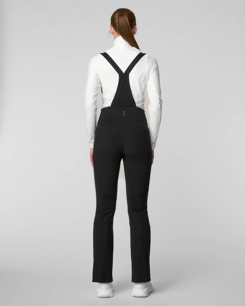 Back view of a woman wearing black bib-style ski pants with suspenders