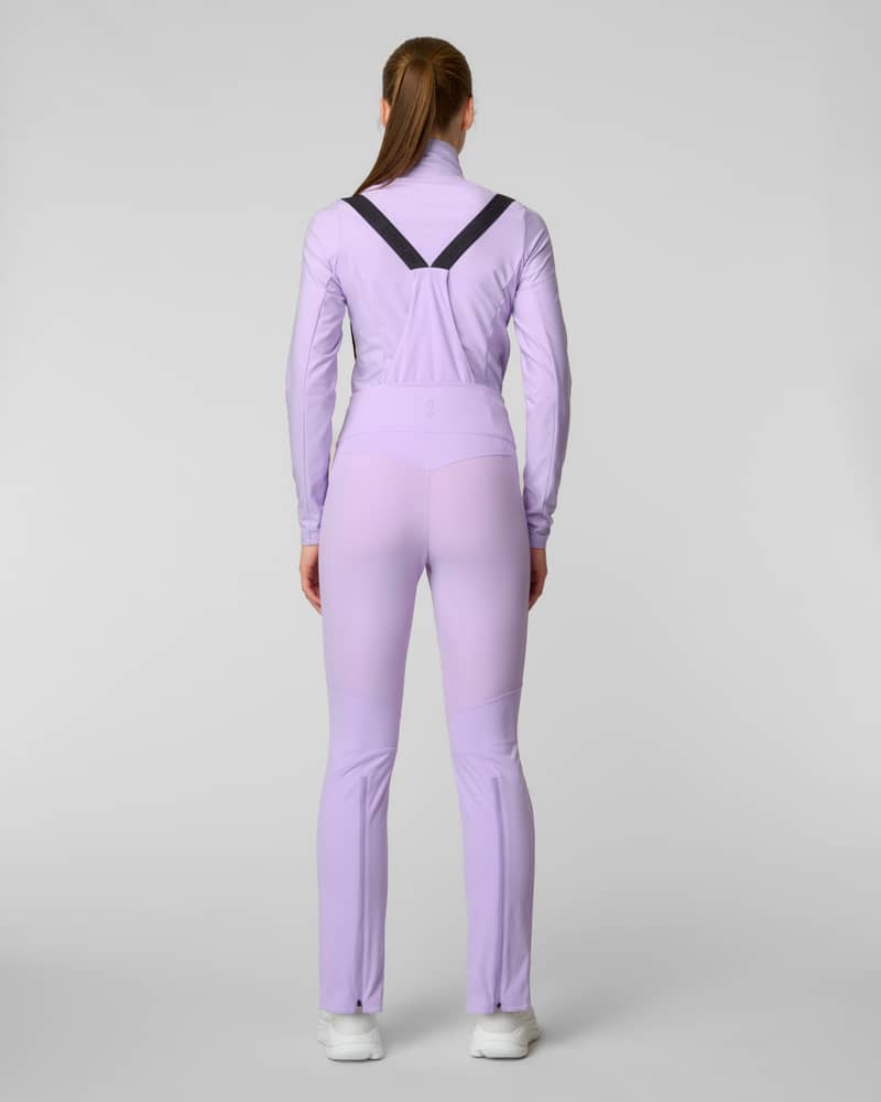 Back view of a woman wearing lavender bib-style ski pants with suspenders