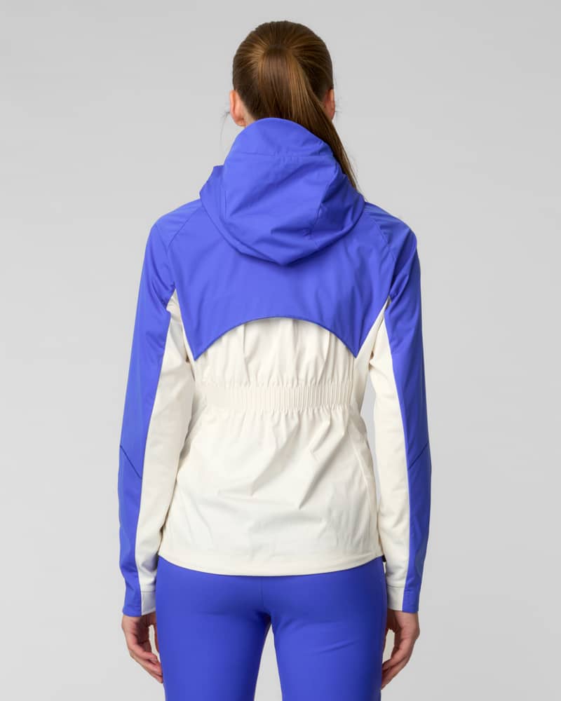 Back view of woman wearing a blue and white colorblock hooded jacket in a walkway